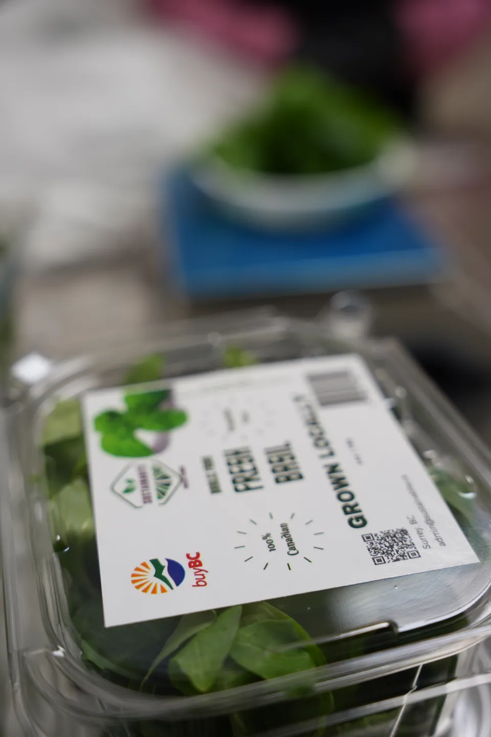A labelled Sustainabite basil pack with green leaves visible inside, beside the packing station.